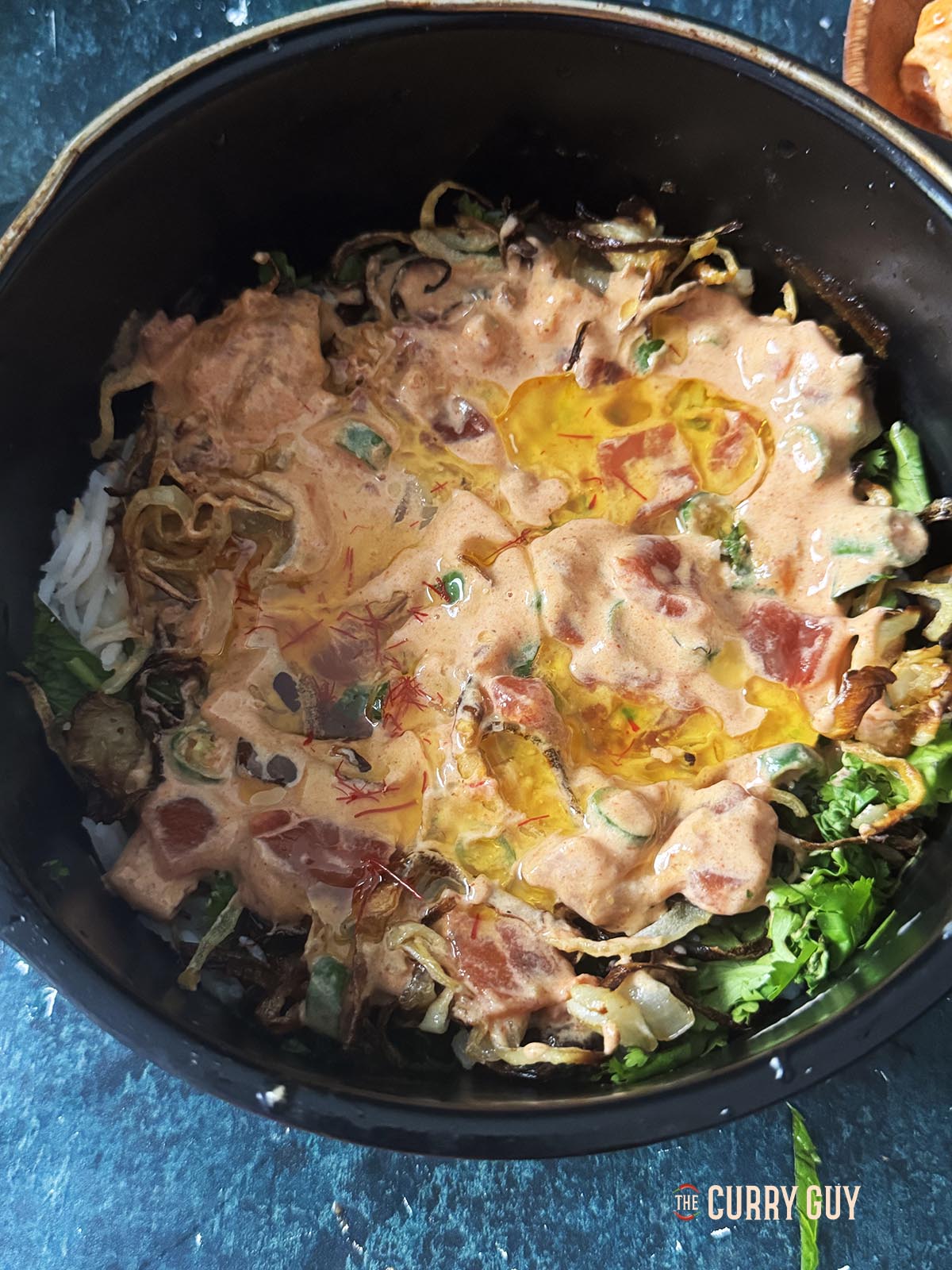 Covering the first layer of the biryani with half of the marinade and melted saffron infused ghee.