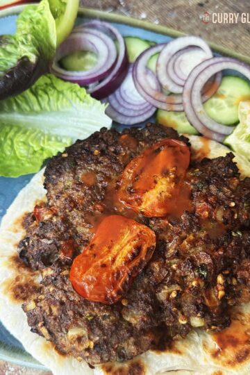 Chapli kebab served on flat bread with vegetables and sauces.