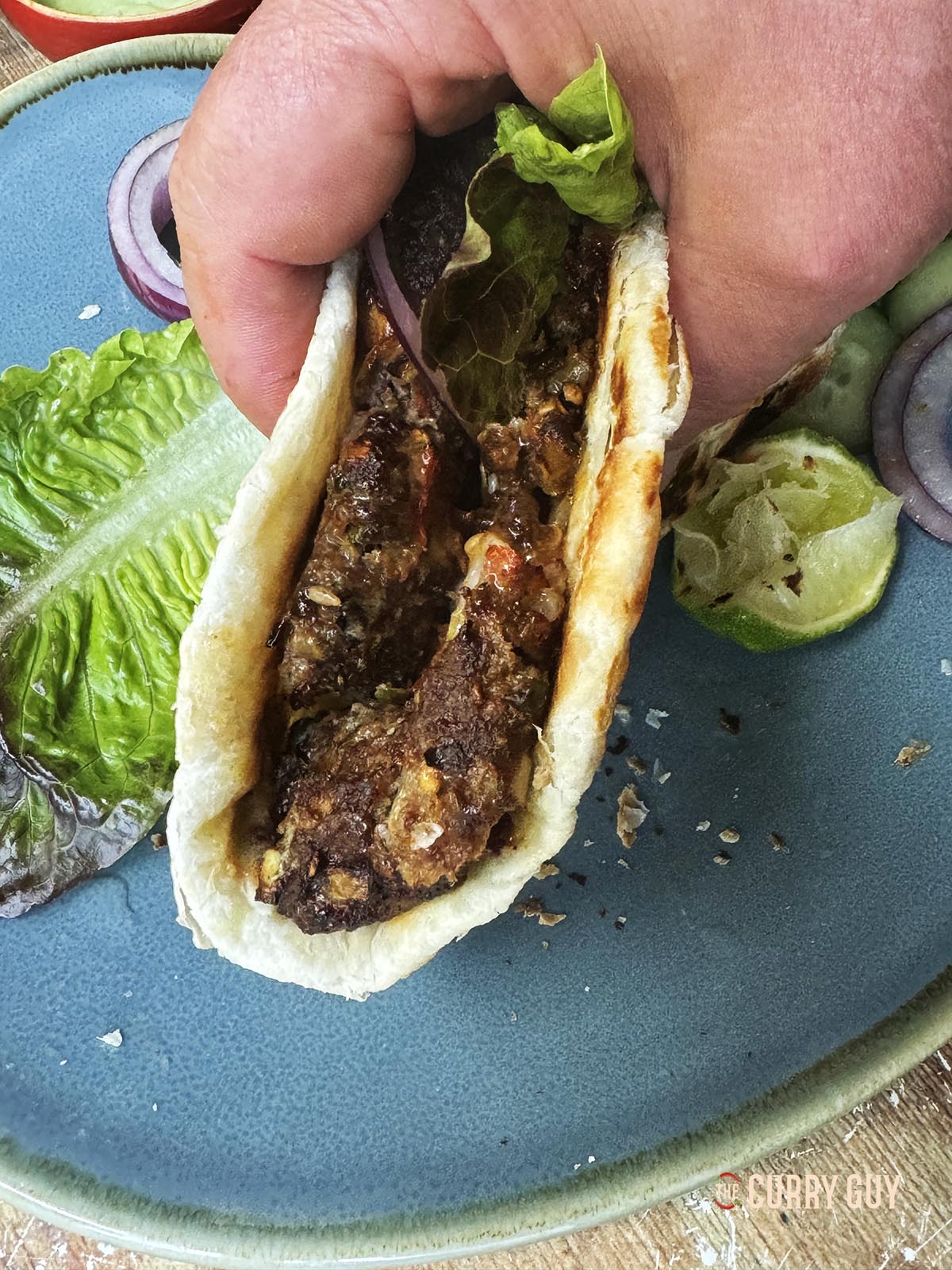 Air fryer chapli kebab wrapped into a flat bread and topped with vegetables and sauce.