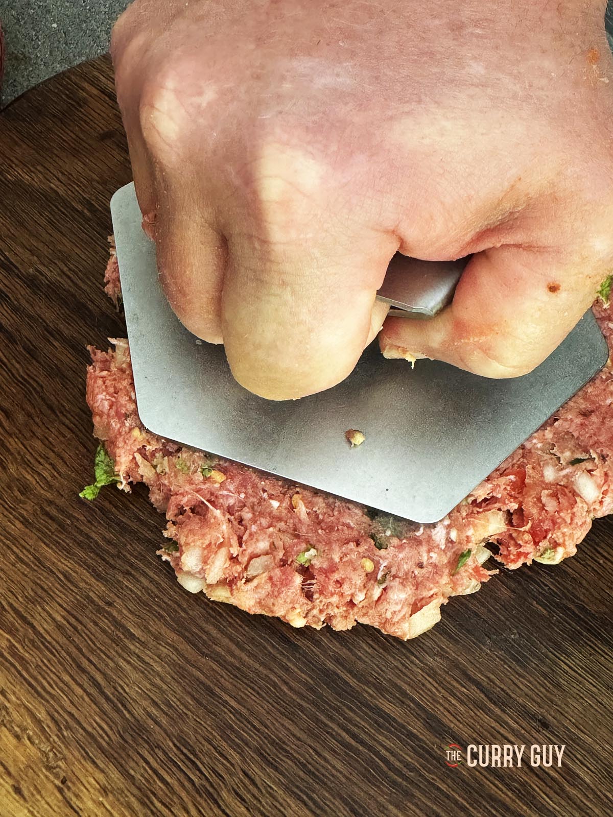 Pressing the kebabs into patties with the sliced tomatoes on top.