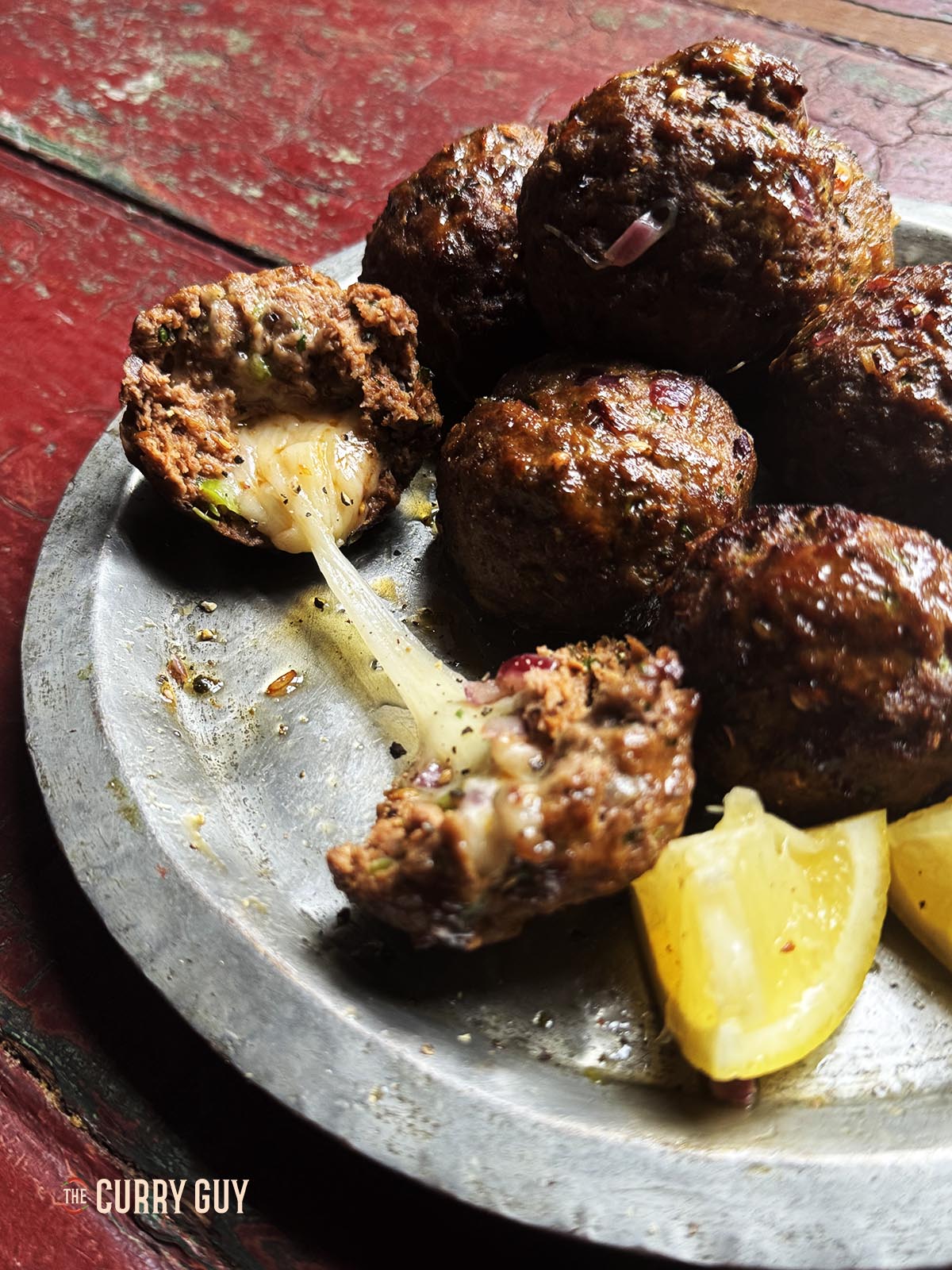 Cheese stuffed meatballs (kofta) on a serving plate with one torn open to show the melted cheese.