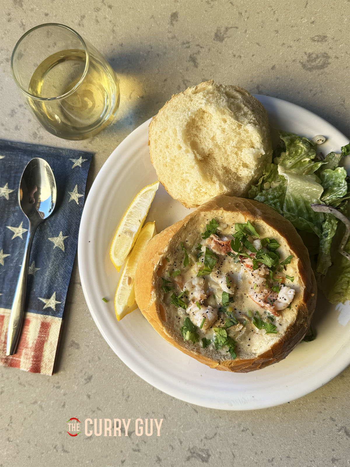 The clam chowder served at the table in a bread bowl, garnished with lobster and fresh herbs.