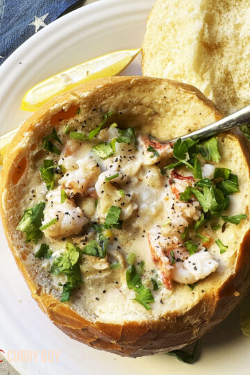Clam chowder on a bread bowl, garnished with herbs and paprika and served with lemon wedges.