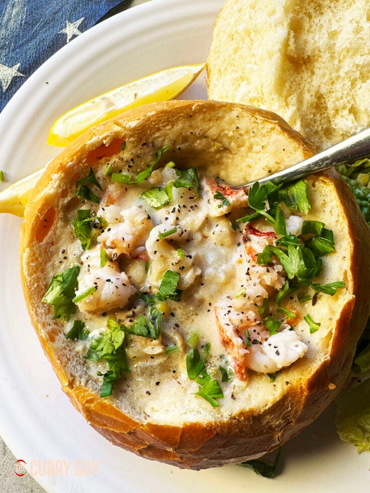 Clam chowder on a bread bowl, garnished with herbs and paprika and served with lemon wedges.