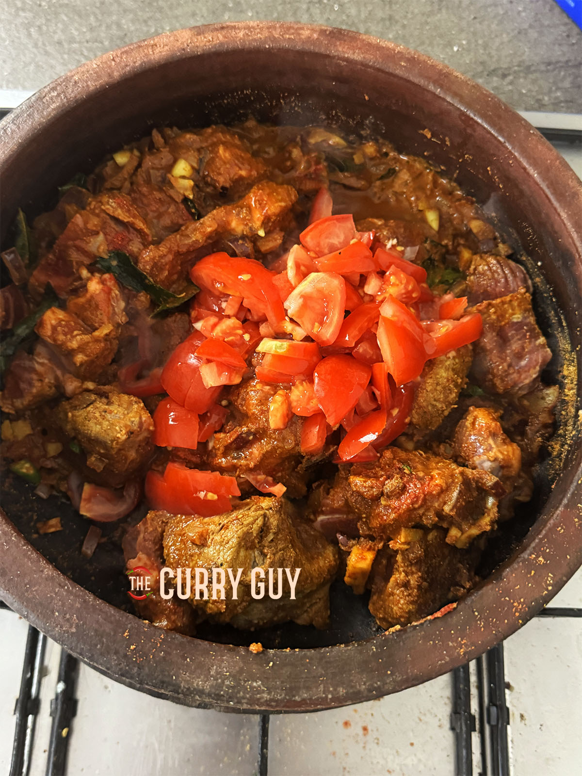 Adding the chopped tomatoes and just enough water to cover the meat to simmer and cook.