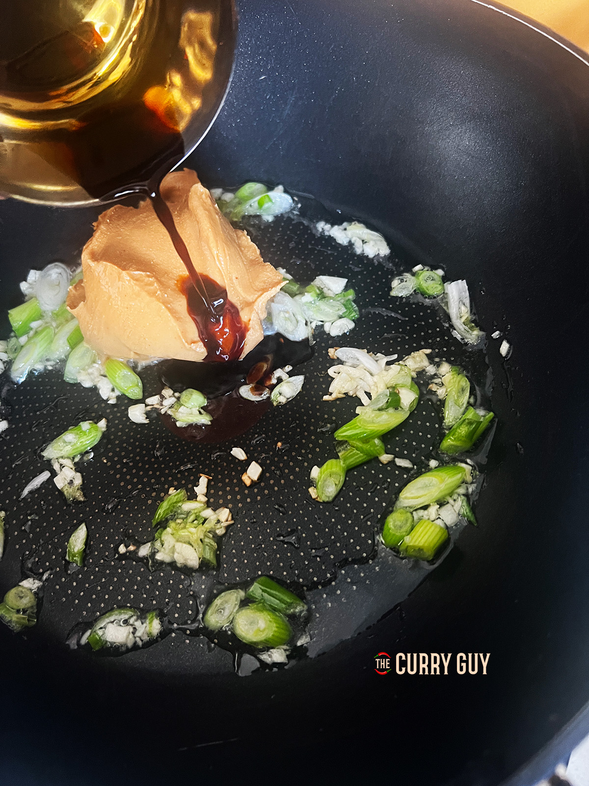 adding the sauce ingredients to the pan for peanut butter noodles