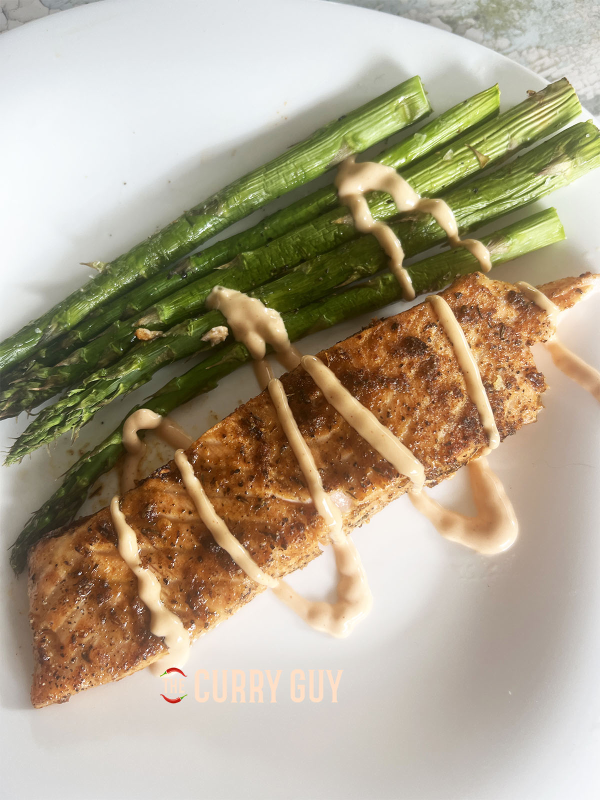 The plated up salmon and asparagus drizzled with some spicy mayo