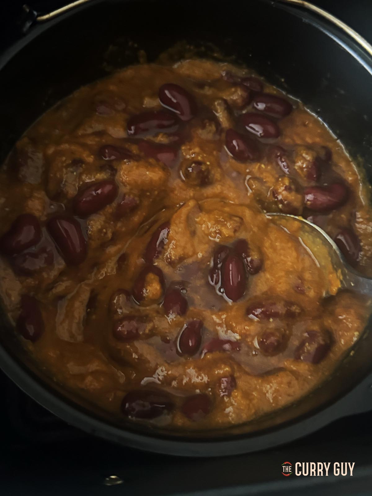 Adding the strained kidney beans to the sauce in the air fryer.