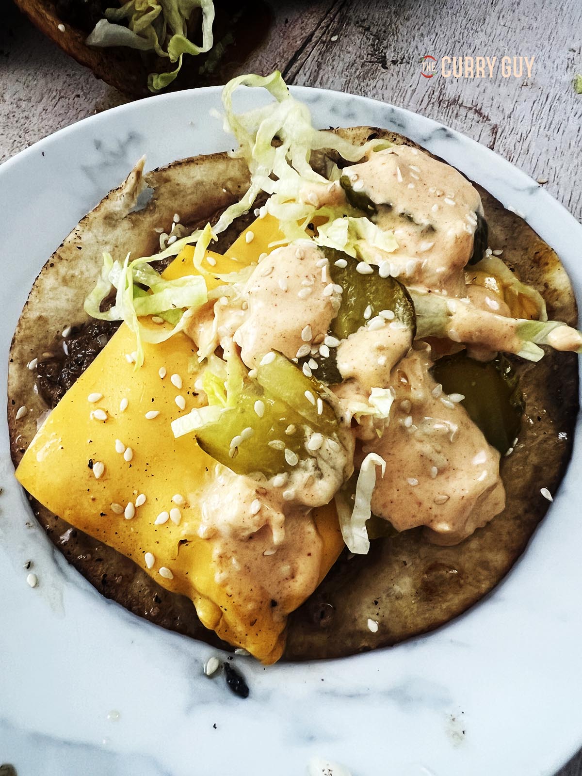 Building a taco by adding lettuce, onion, pickles, sesame seeds and Big Mac sauce.