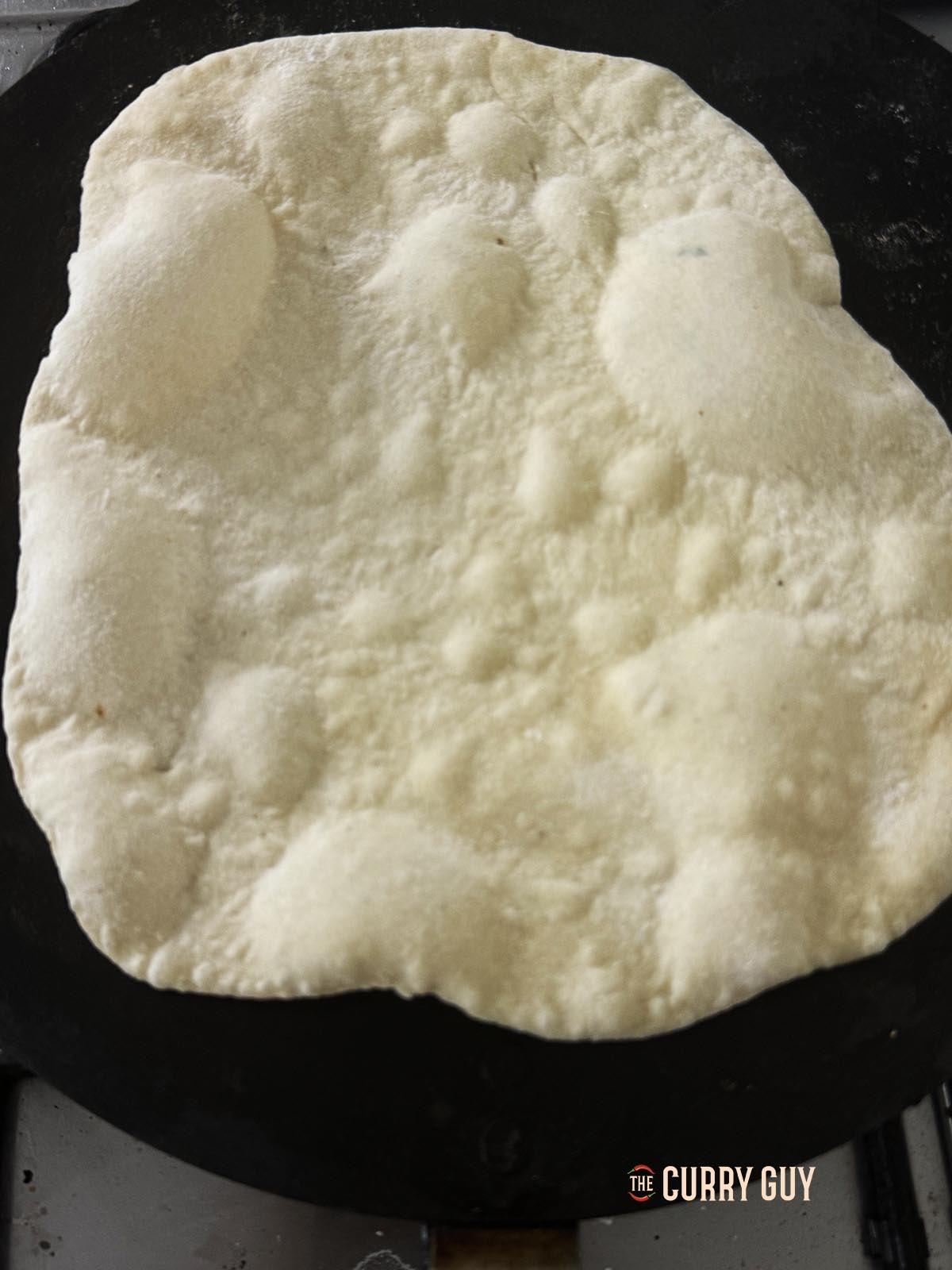 Cooking a lavesh on a tawa. Bubbles are beginning to form on top.