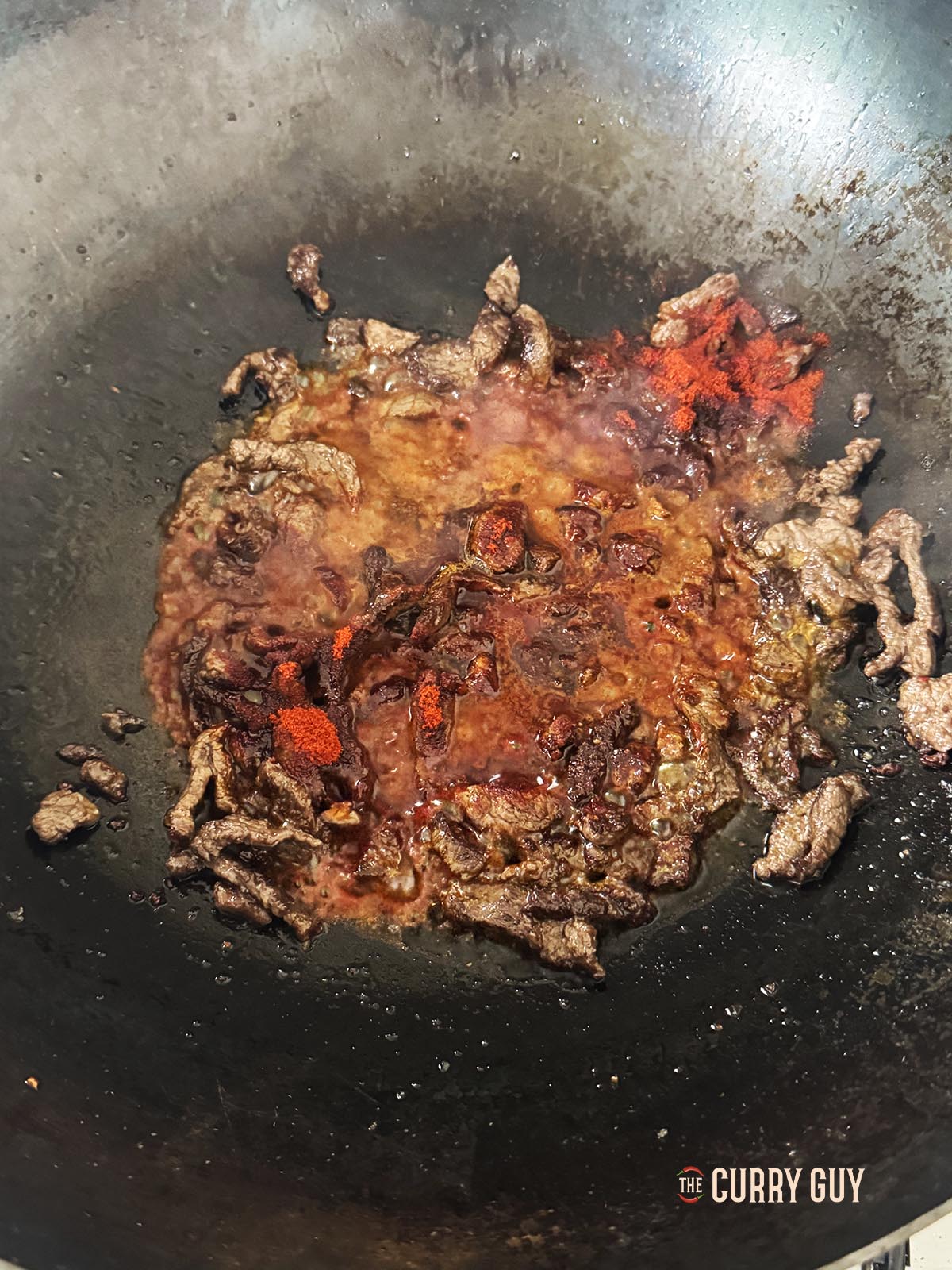 Adding paprika, dried chilli flakes, salt and some of the braising liquid to the meat as it fries.