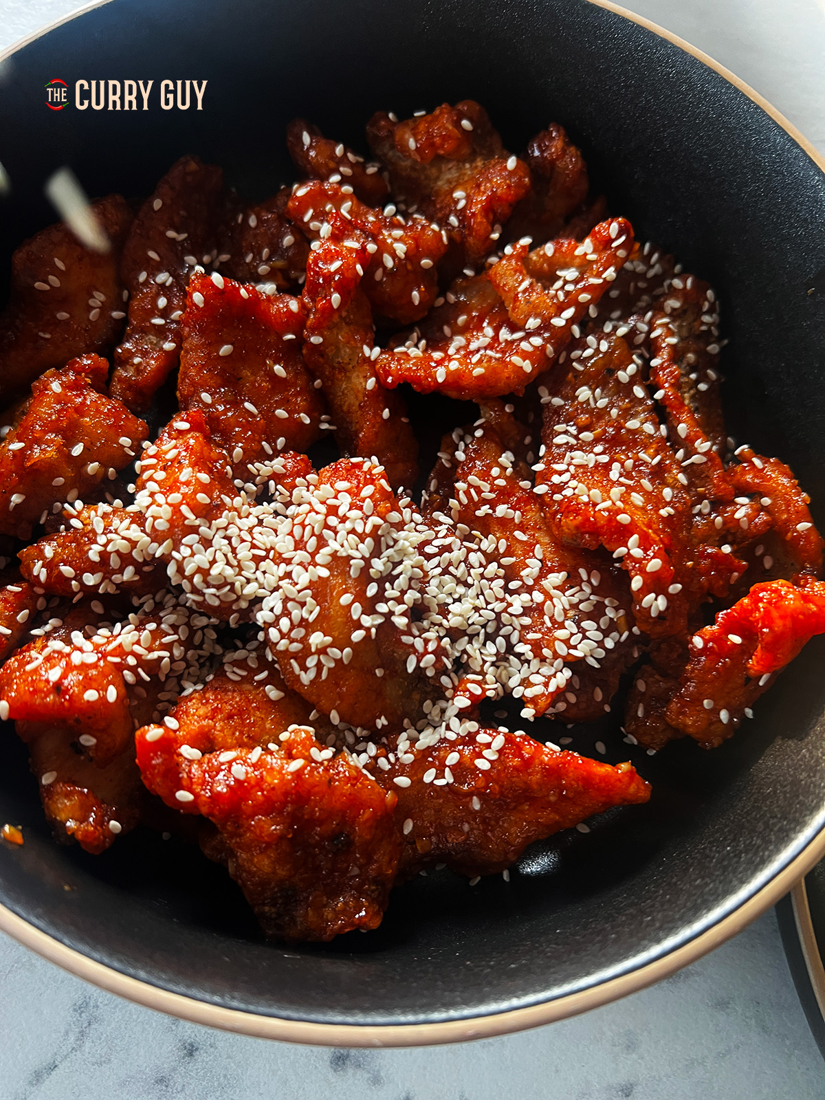 Chicken coated in the sauce and topped with sesame seeds. 