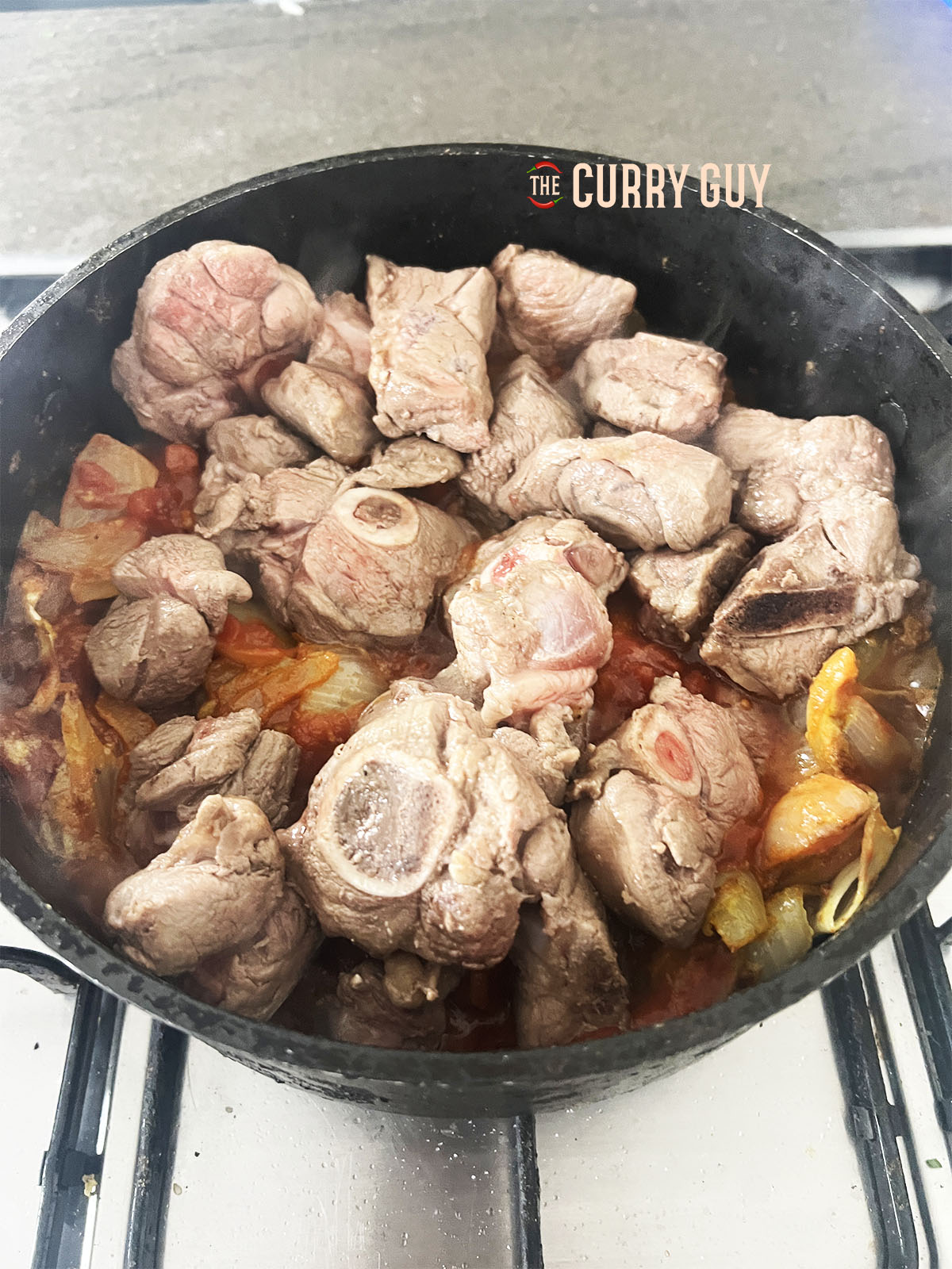 Returning the browned meat to the pan. 