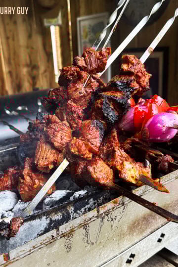 Beef shish kabobs smoking on skewers over hot coals.