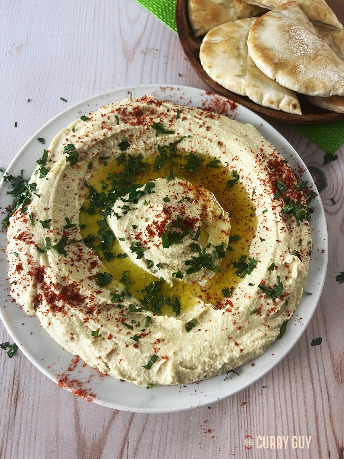 Hummus that was prepared using this easy hummus recipe. The hummus is served on a serving plate, garnished with parsley, aleppo chilli powder and extra virgin olive oil. 
