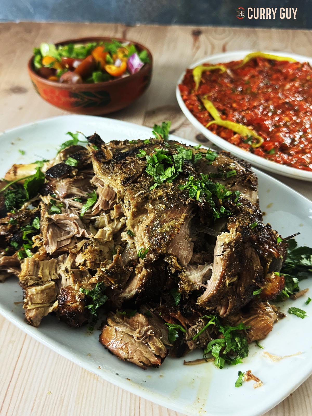 Slow cooked lamb on a serving platter with salads in the background.