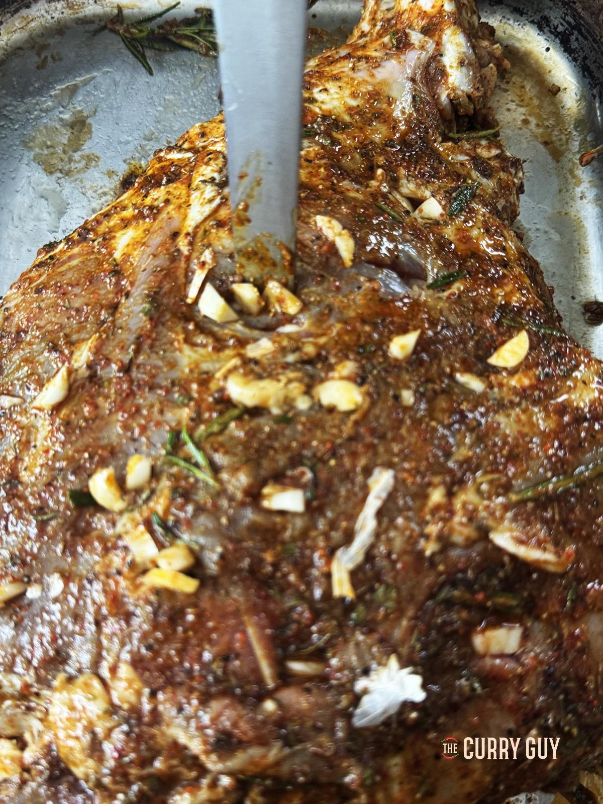 Making holes in the lamb and placing garlic slivers in them. 