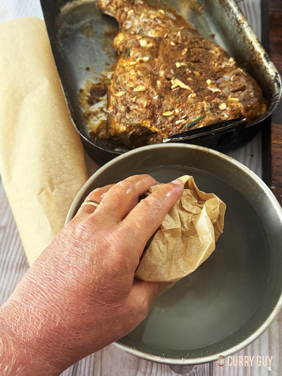 Dampening parchment paper on water to wrap the lamb before roasting.
