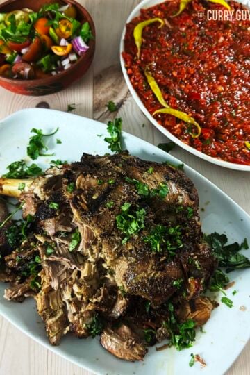 Slow cooked lamb on a serving platter with ezme salad and green salad side dishes.