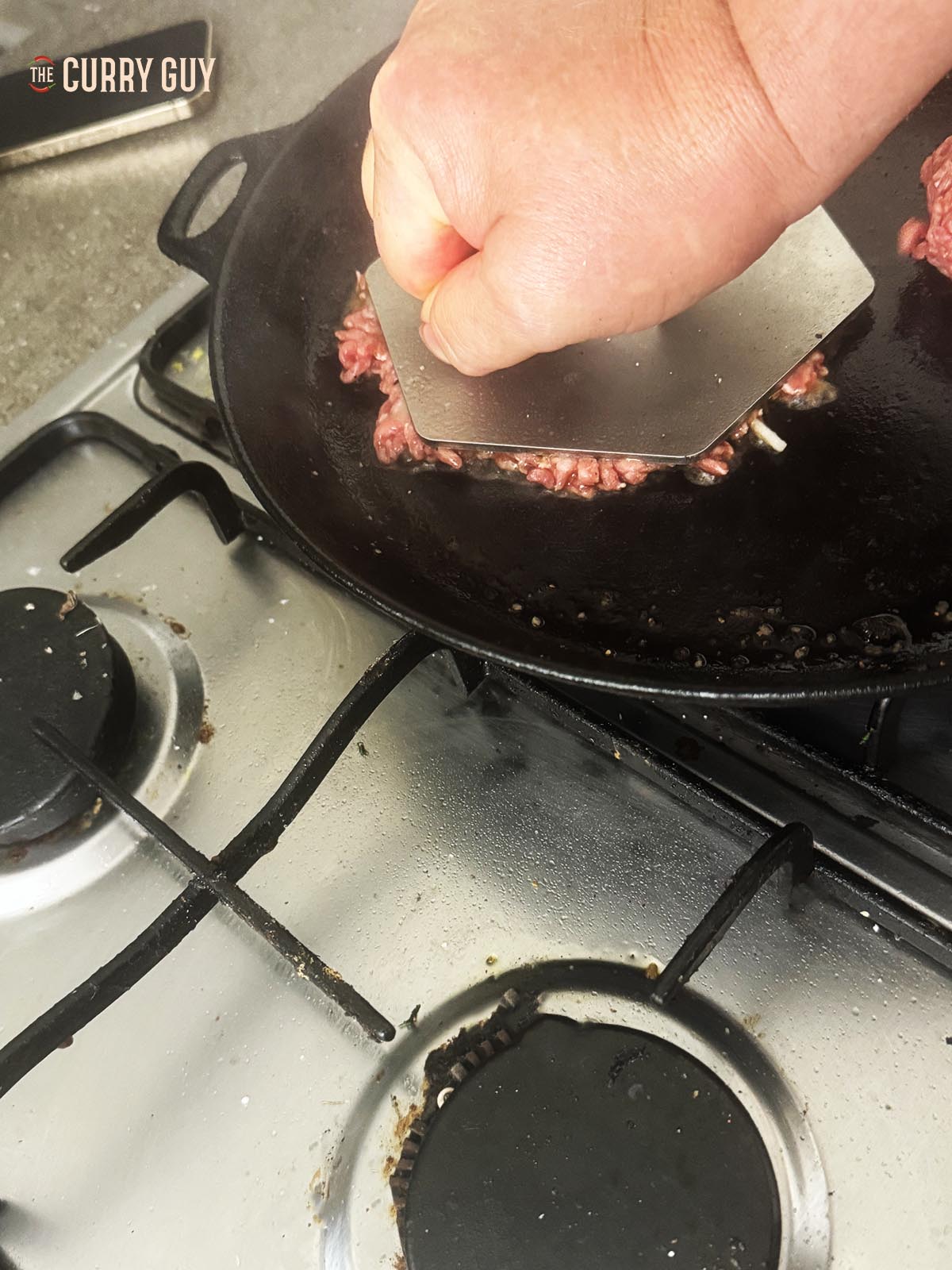 Smashing the burgers with a burger press in the pan.