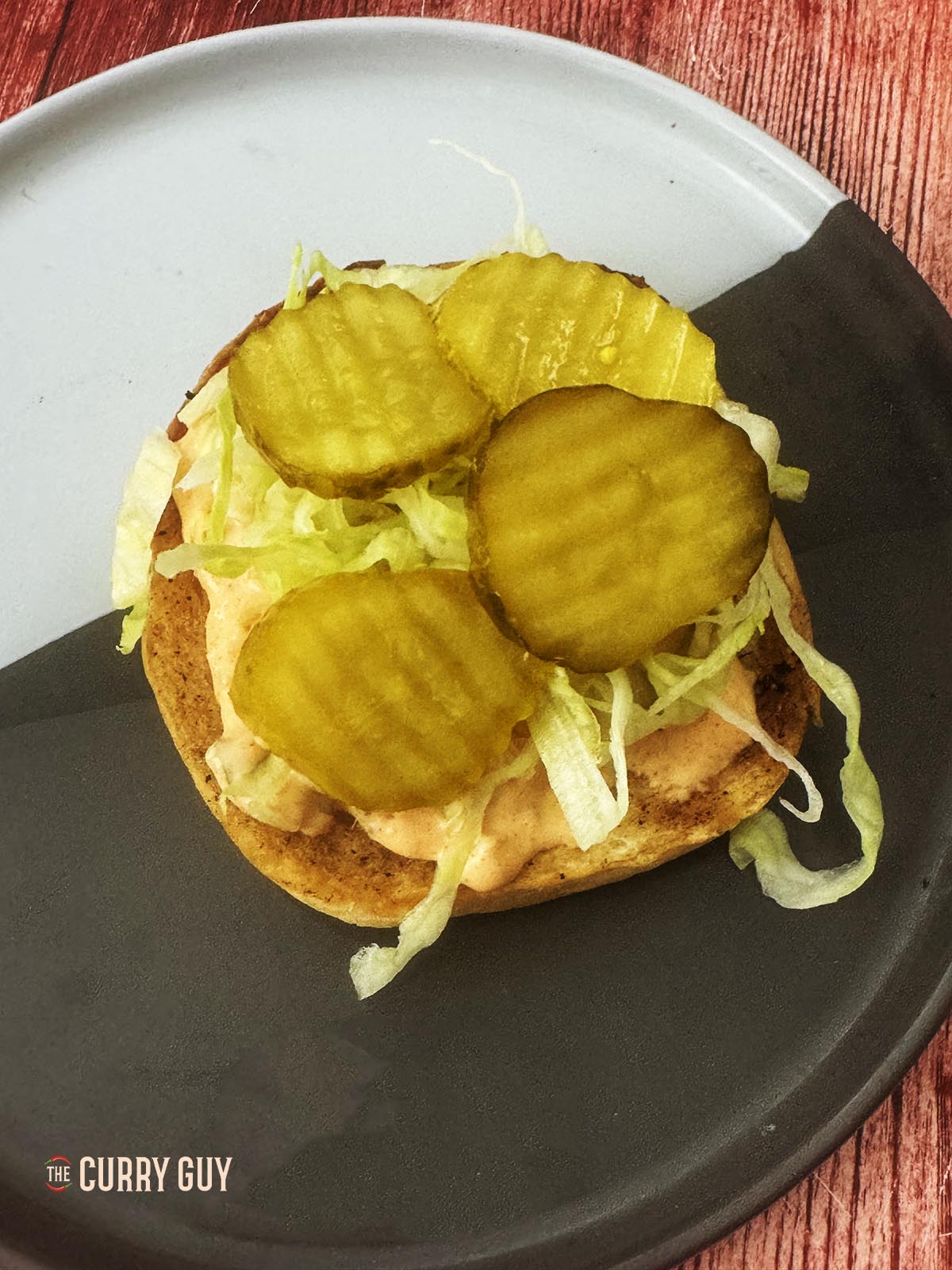 Adding shredded lettuce and pickle slices to the bottom bun.