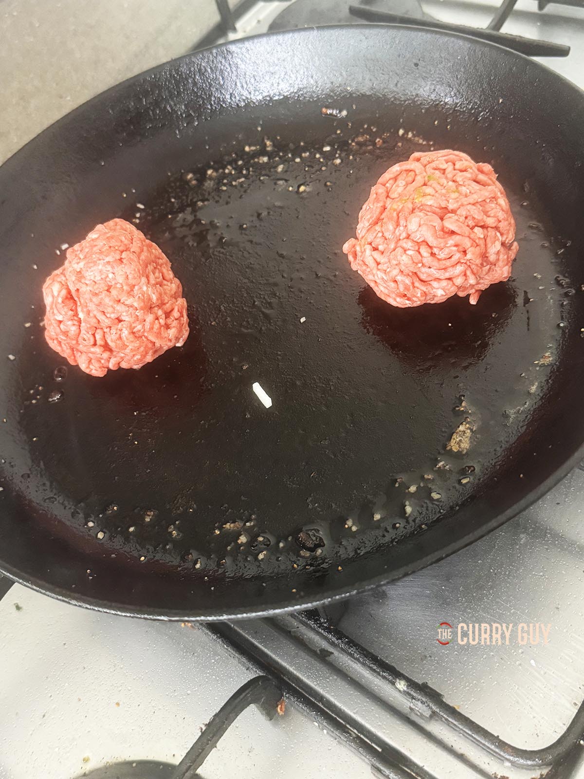 Placing burger balls in a smoking hot pan to cook. 