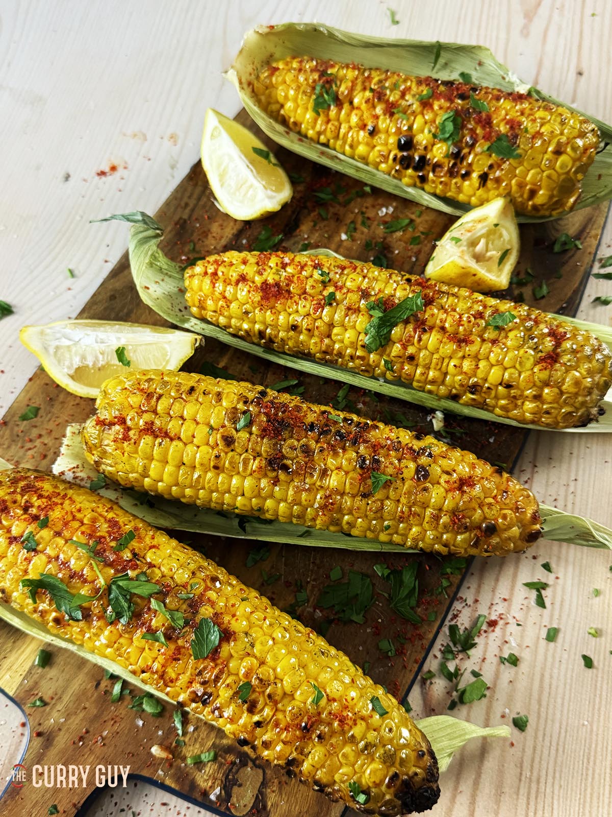 The grilled corn on the cob, served on the green husks and seasoned with salt, chilli powder, chopped parsley and lemon juice. 