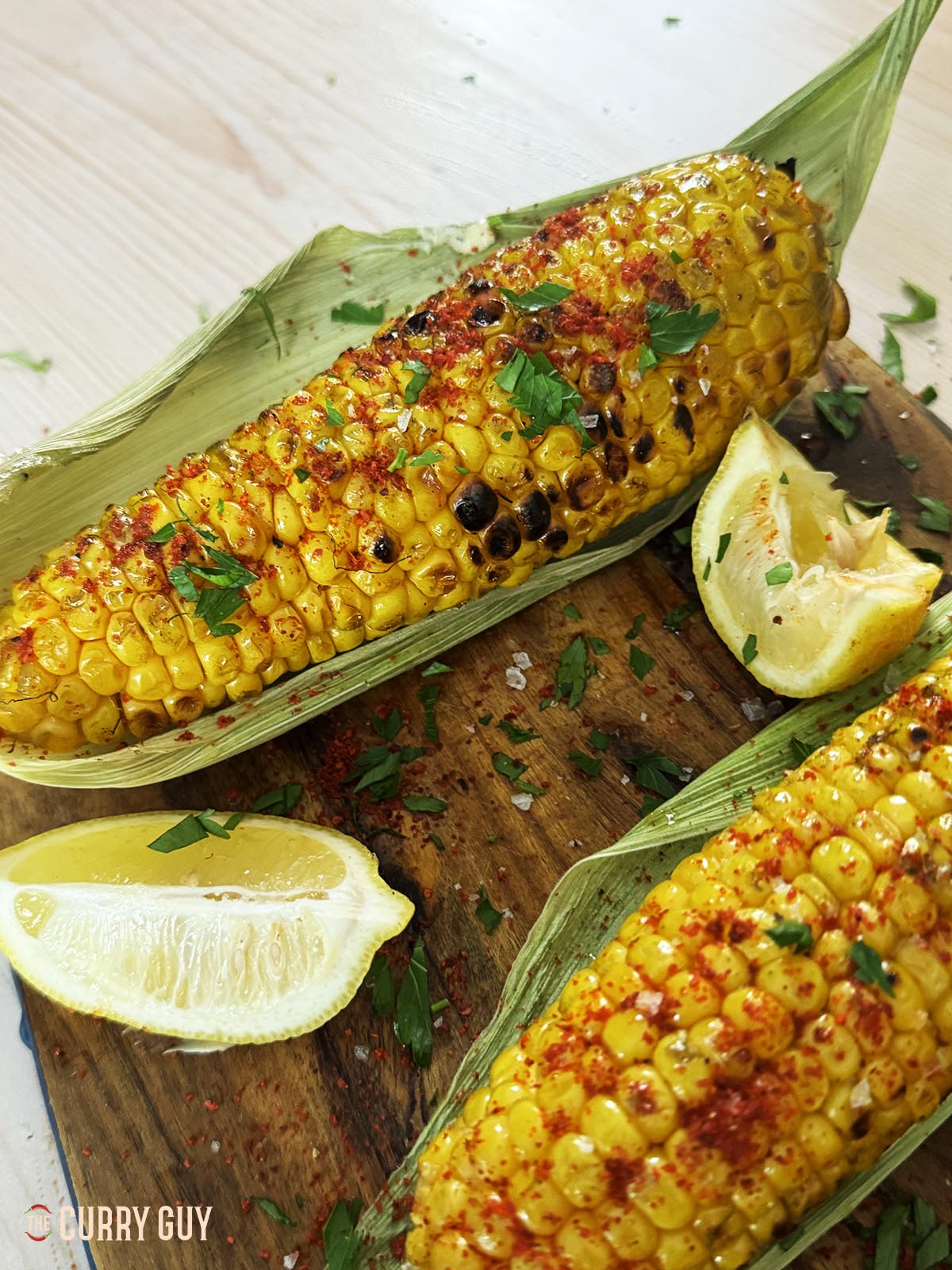 Grilled corn on the cob seasoned with salt, chilli powder, chopped parsley and lemon juice. Served on green corn husks.