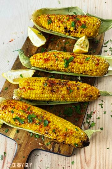 Grilled corn on the cob served with spices, salt and parsley on a serving platter.