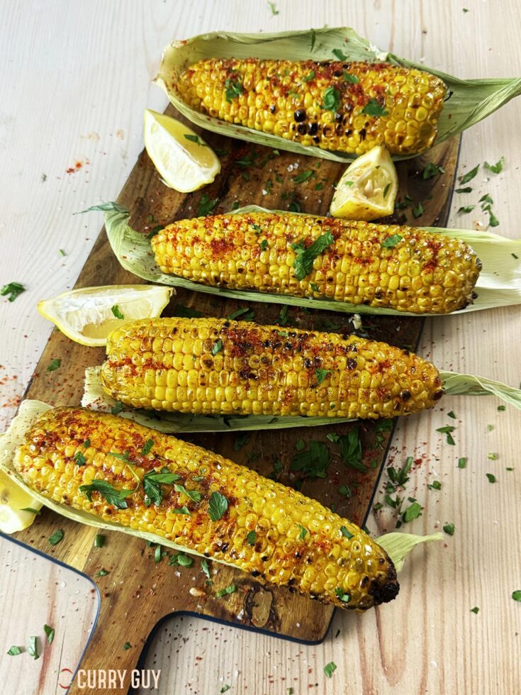 Grilled corn on the cob served with spices, salt and parsley on a serving platter.