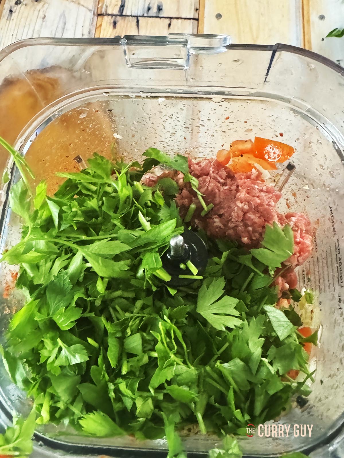 Adding parsley and meat to the blender to blend into the meat paste.