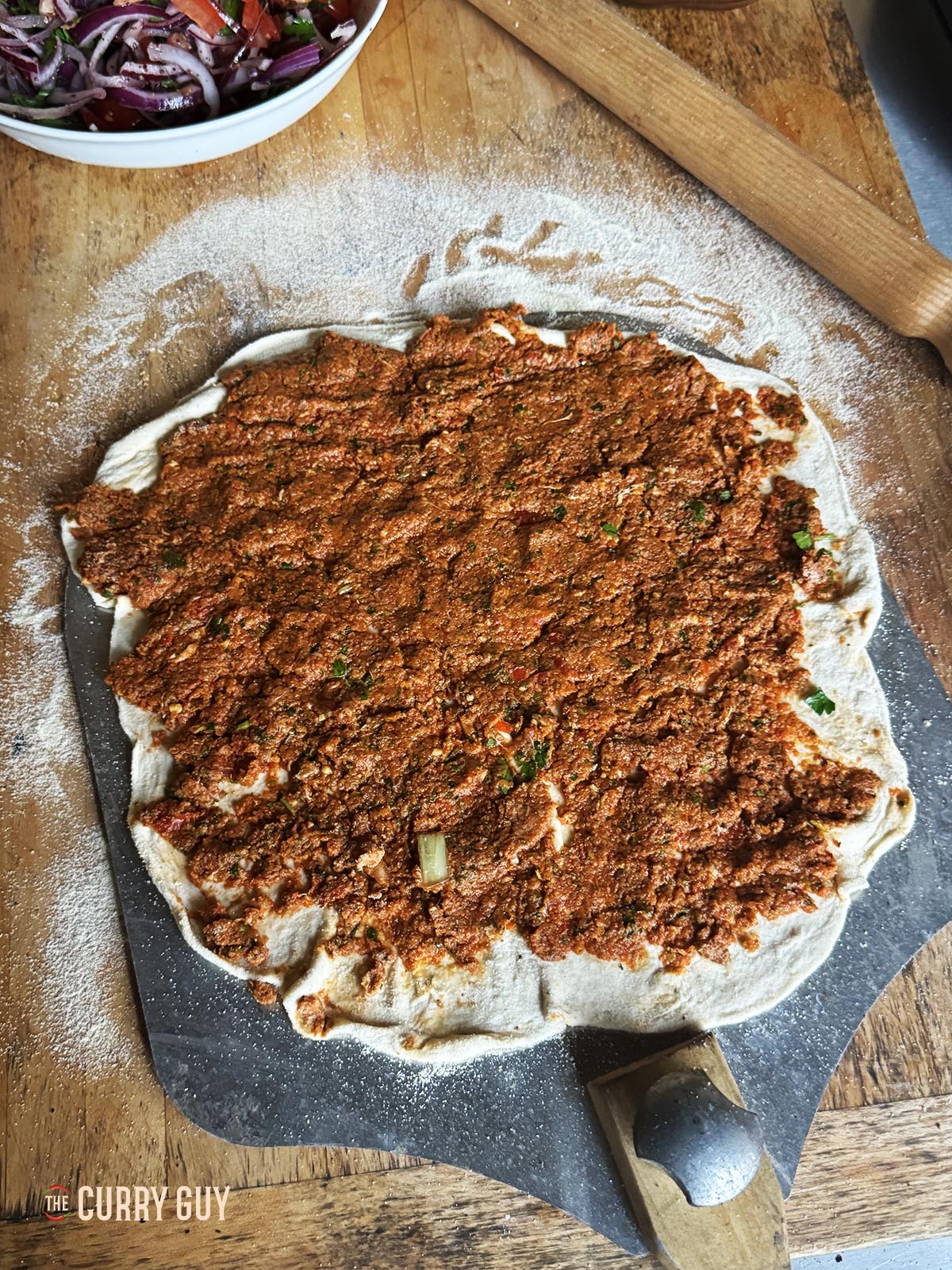 Meat paste spread all over a flatbread, ready to cook. 