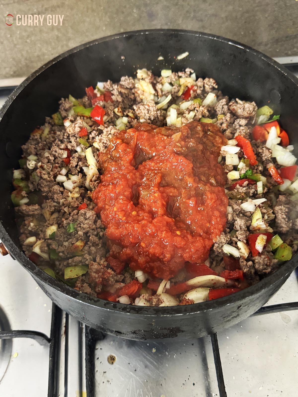 Adding the chopped tomatoes to the meat.