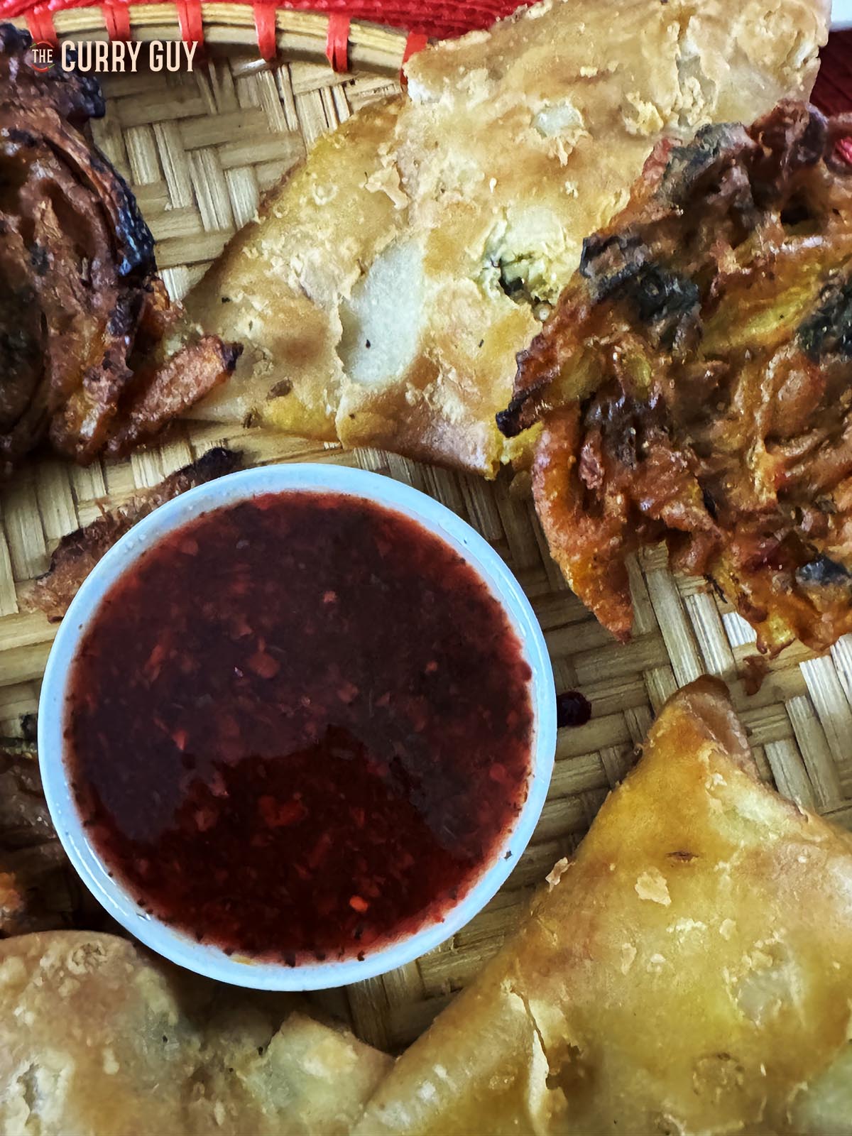Red samosa dipping sauce in a bowl next to samosas and onion bhajis.