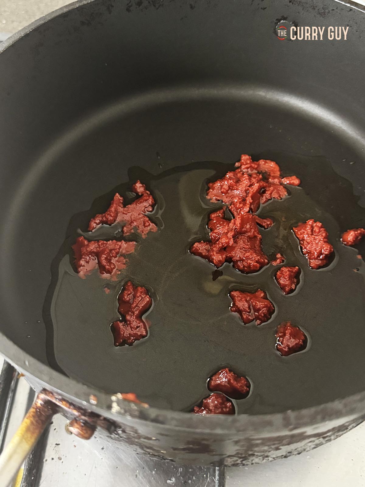 Frying tomato paste over a medium heat in oil in a frying pan.