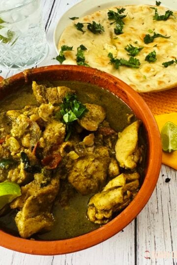 Spicy chicken curry in a serving bowl with a side of naans.