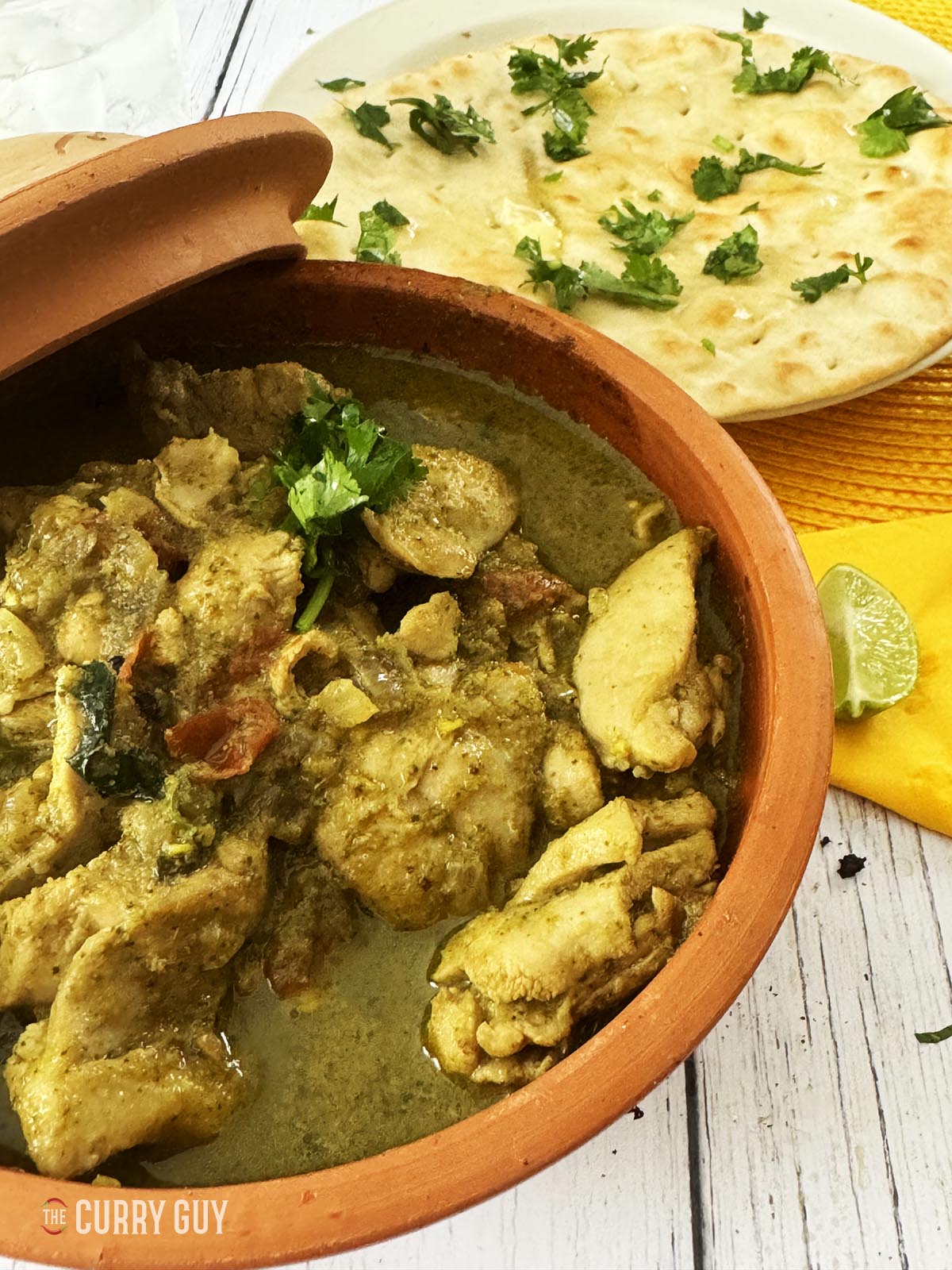 Spicy chicken curry in a serving bowl with naan side dish.