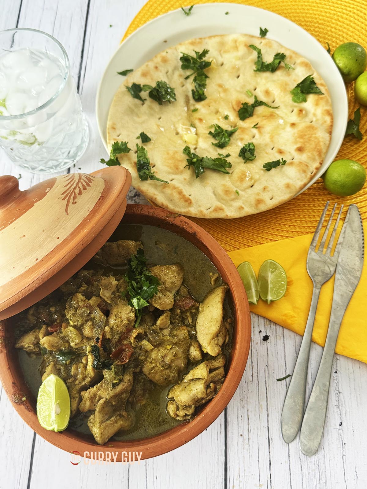 Spicy chicken curry served in a bowl at the table with a side of naans.