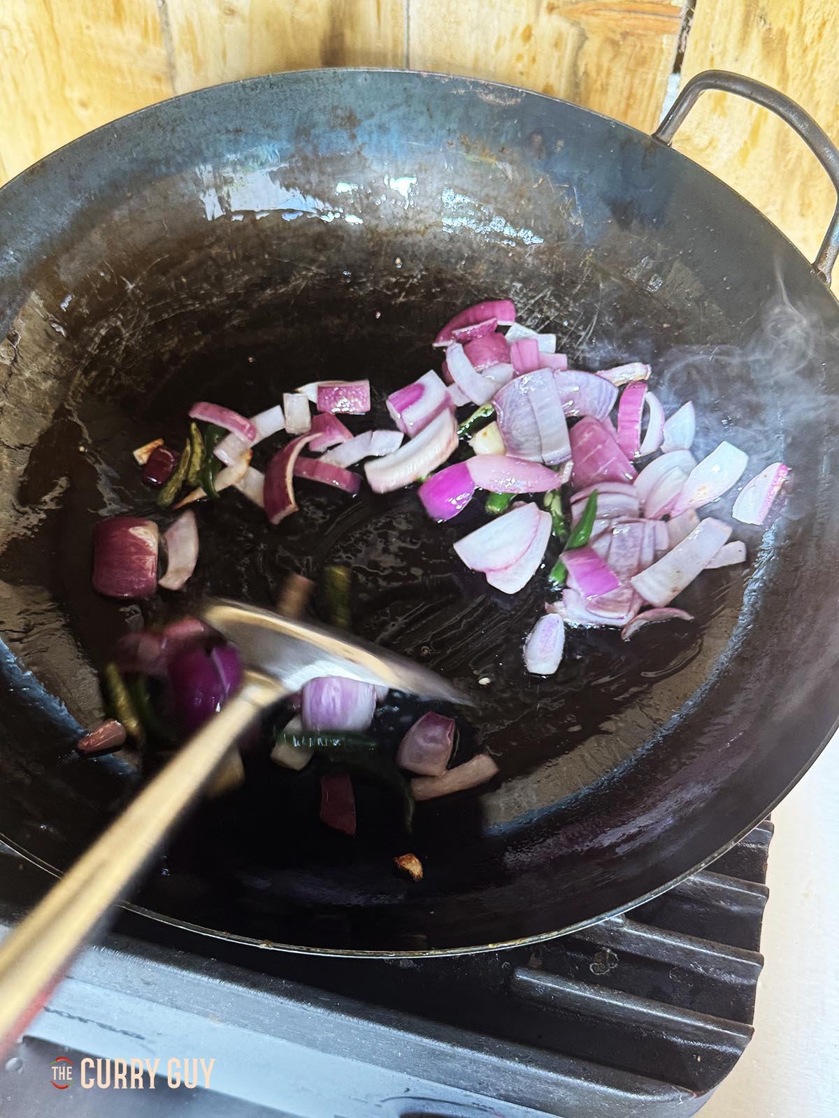 Frying the roughly chopped onions, garlic and chillies in a wok. 