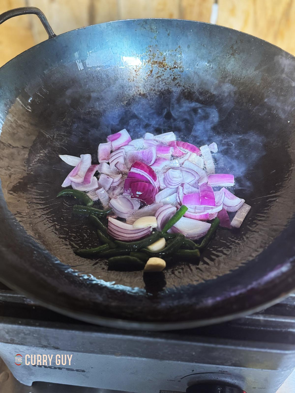 Adding the chopped onions, garlic and chillies to hot oil in a wok.