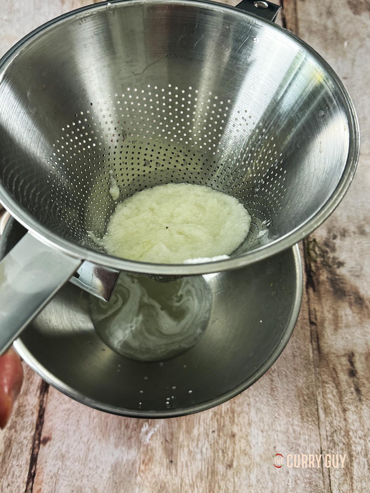Running the blended onion and garlic paste through a sieve to get the juice out.