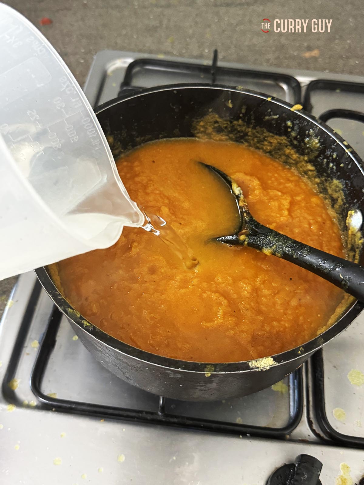 Adding water to the sauce in the pot.