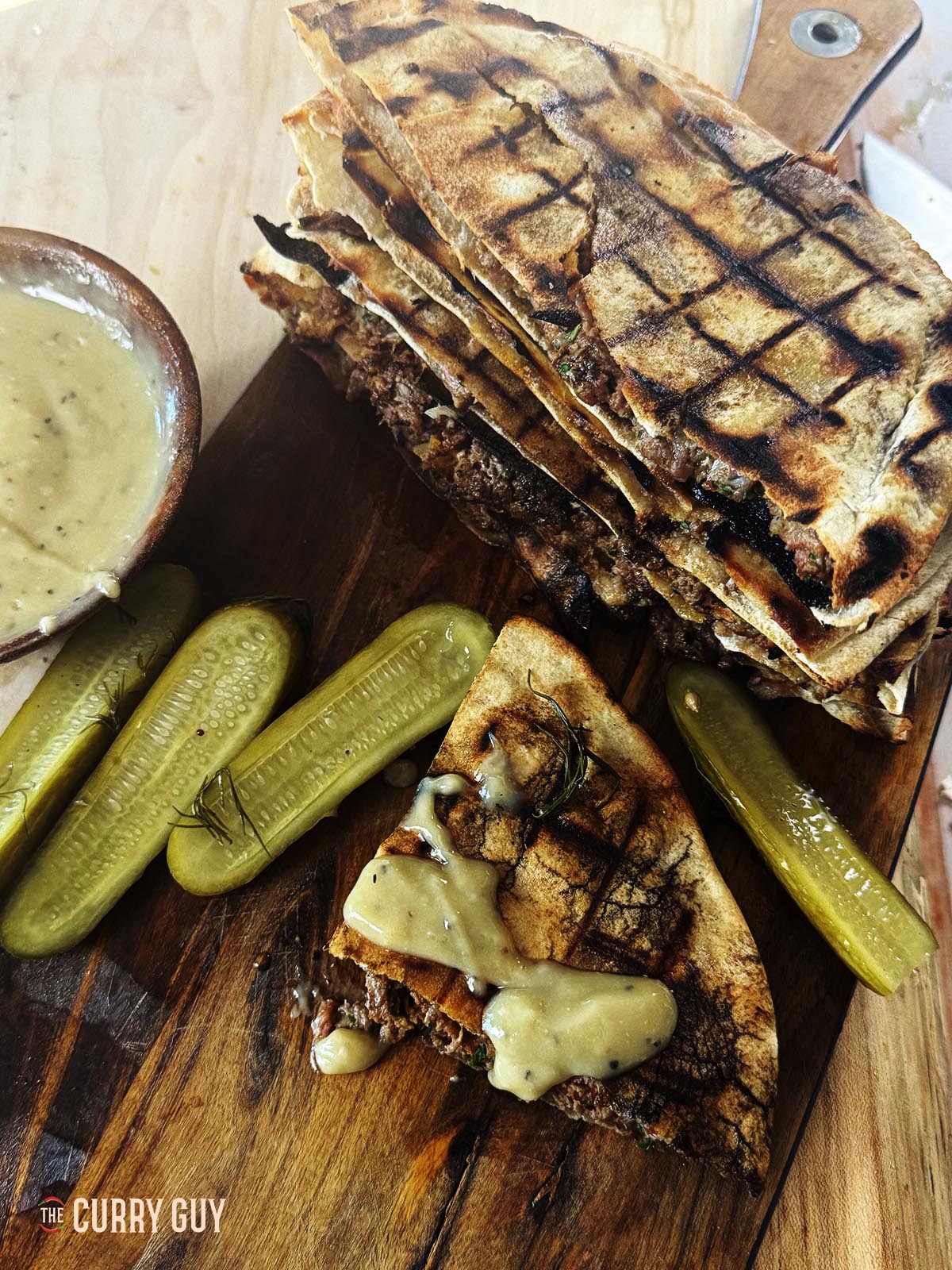 Meat stuffed pitas (Areyes) on a serving platter with pickles and tahini sauce.