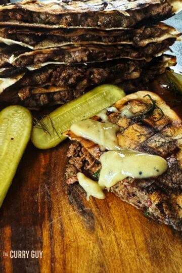 Meat stuffed pitas (areyes) on a serving platter topped with tahini sauce.