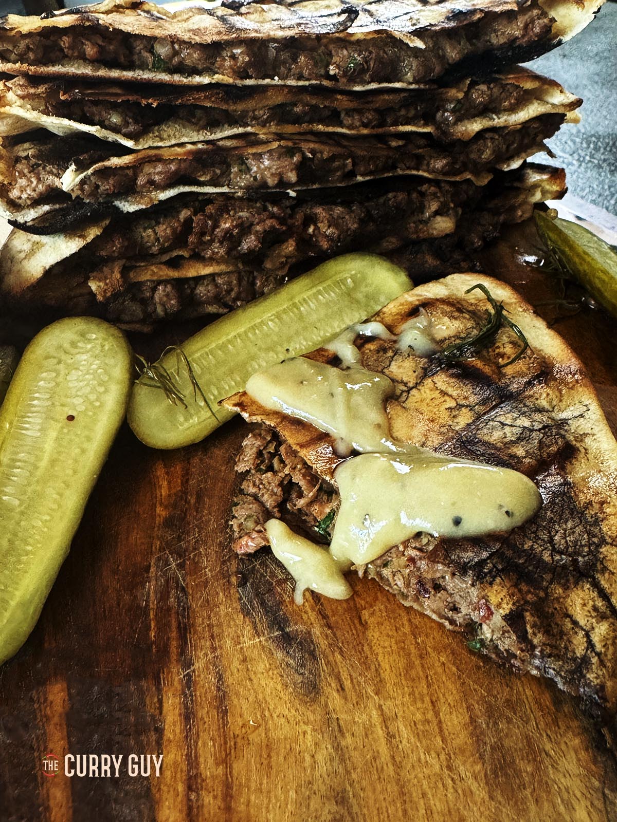 Meat stuffed pitas (areyes) on a serving platter topped with tahini sauce.