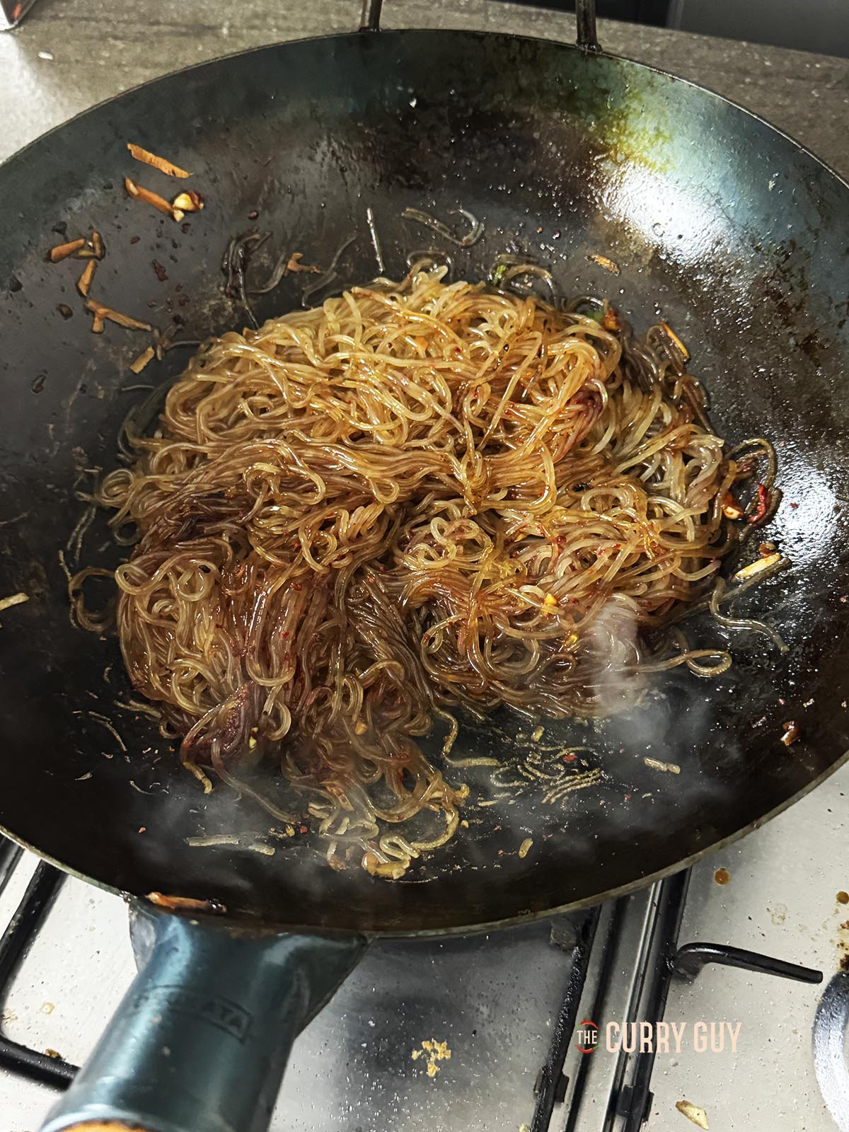 Adding the sauce to the noodles in the wok.