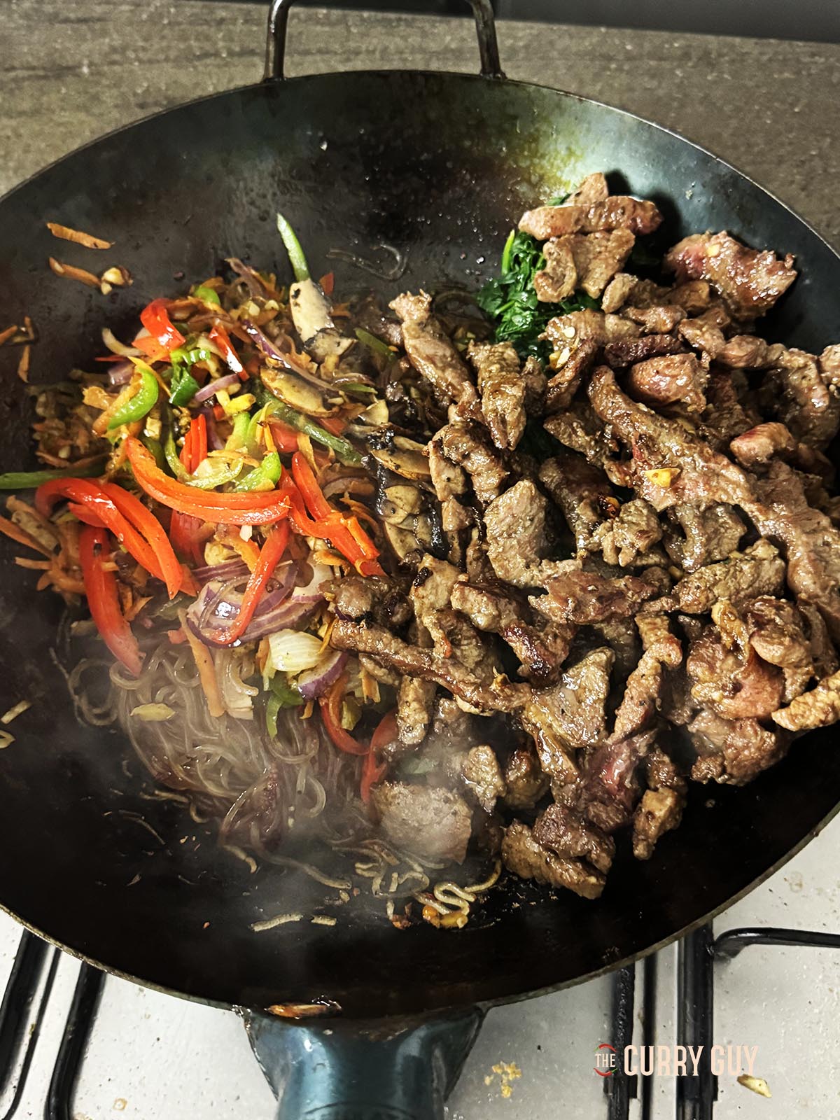 Adding the previously cooked ingredients to the noodles.