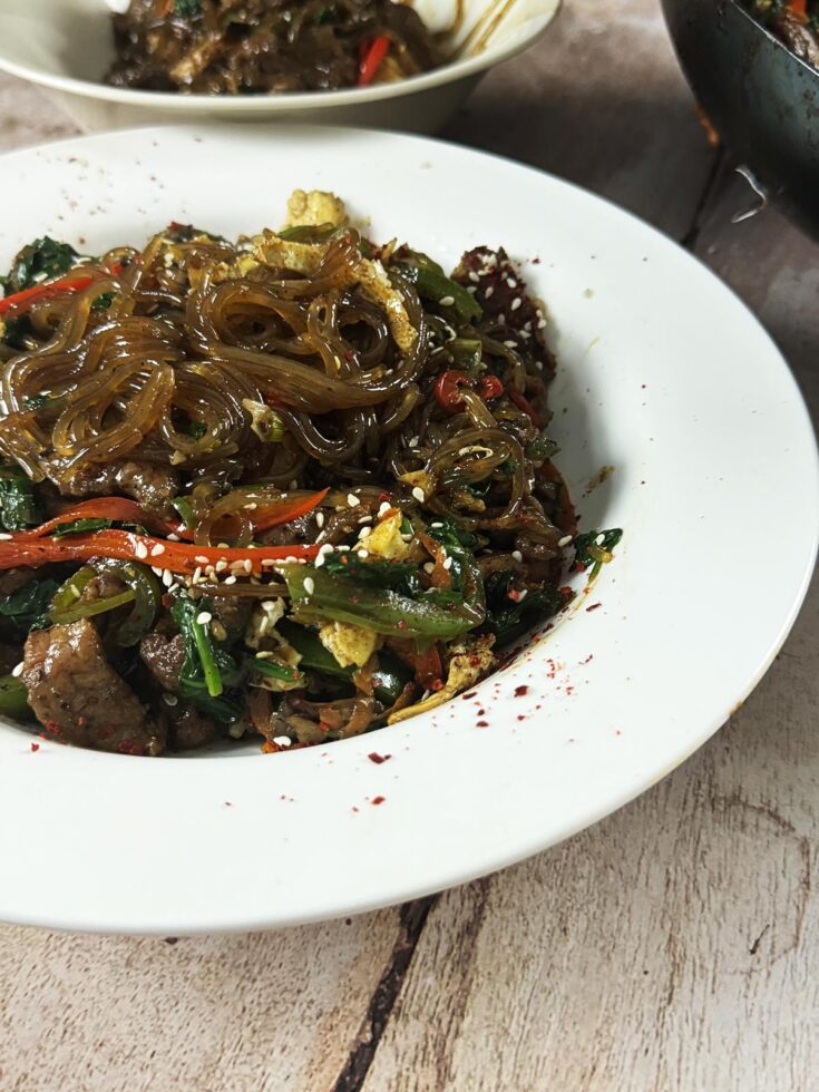 The finished japchae recipe in a serving bowl at the table.