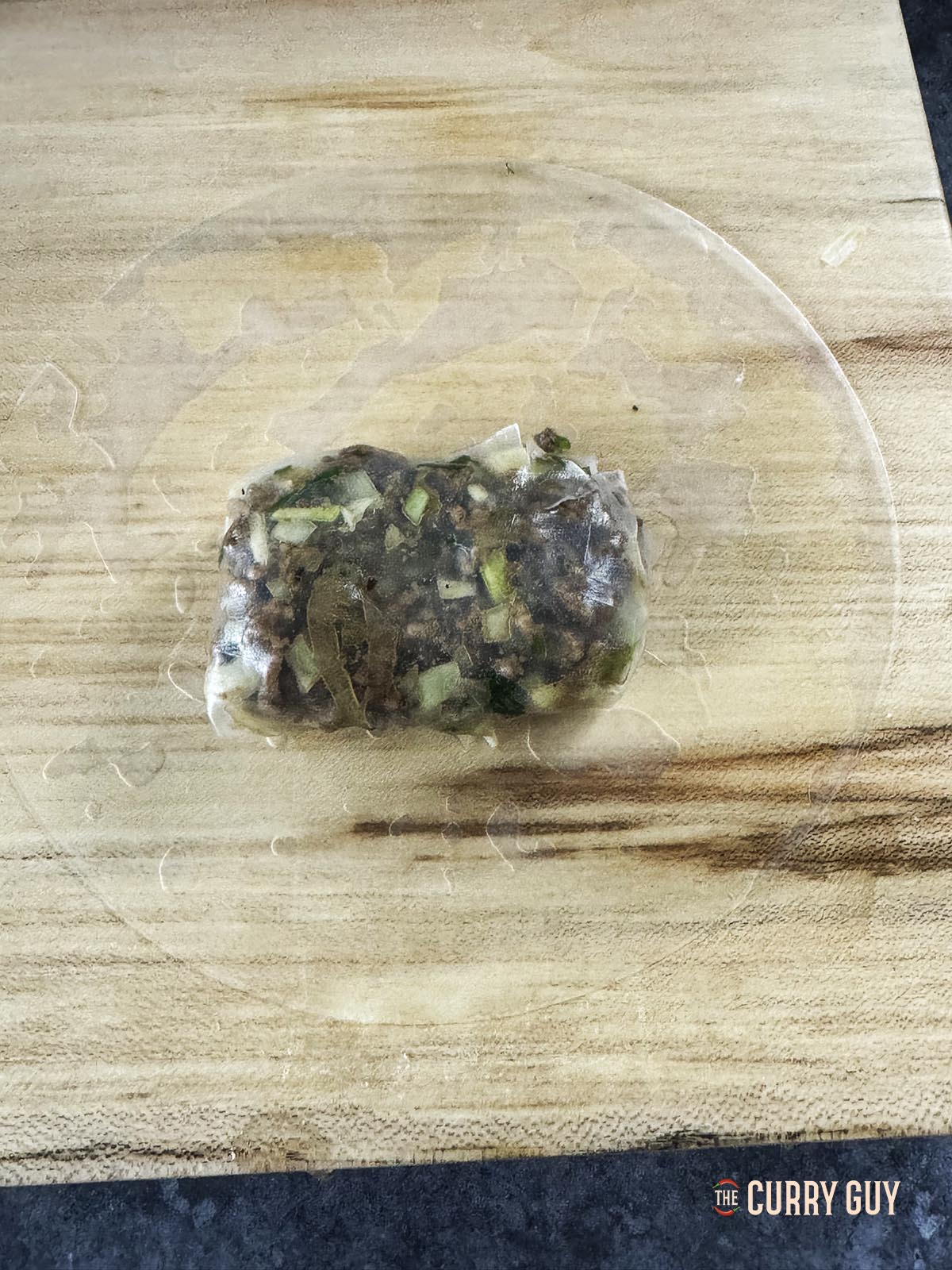 Placing the meat wrapped in rice paper on another piece of rice paper to double encapsulate the meat in rice paper.