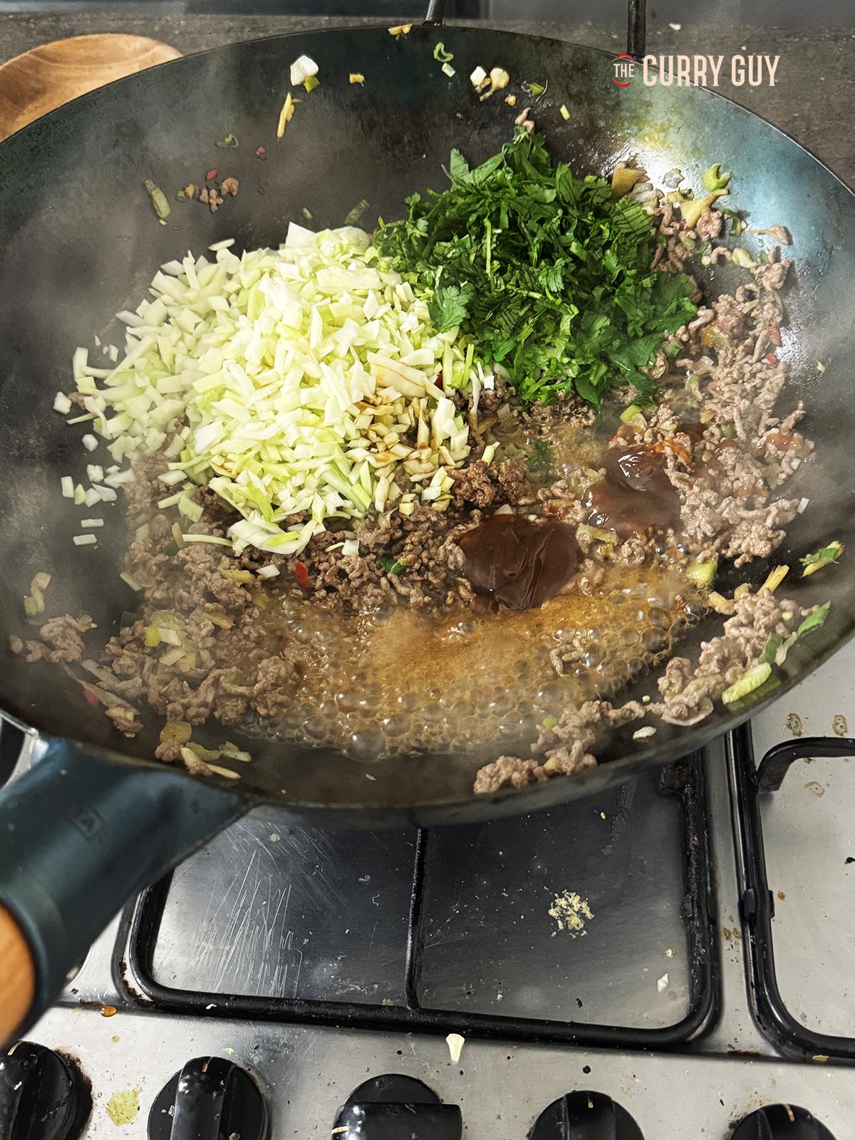 Adding the cabbage, coriander (cilantro), soy sauce and oyster sauce to the wok.